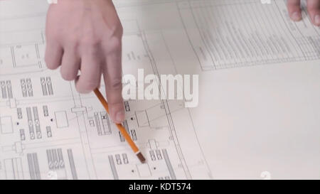 A man shows using a pencil on a drawing or blueprint on the table. Man show construction plans at the table. Business man Architect or engineer show their working architecture model in office. Stock Photo