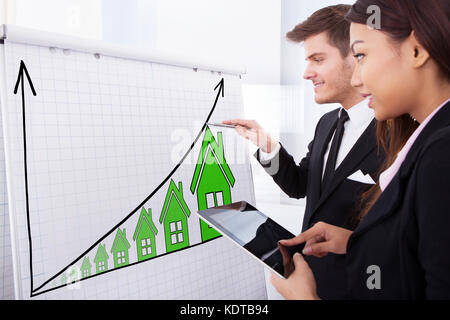 Two Successful Businesspeople Working On House Raise Concept On Flipchart Using Digital Tablet Stock Photo