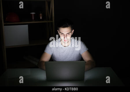 Architect sitting at night working on architectural plan on laptop. Young interior designer in casual checking blueprint of a house on laptop. Stock Photo