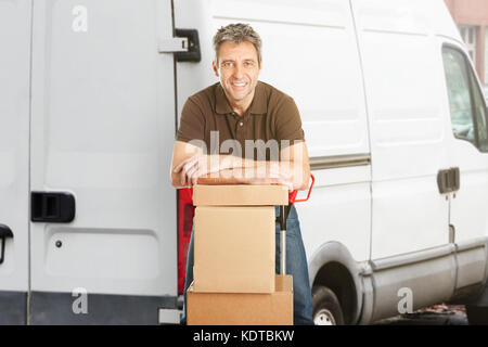 Smiling Delivery Man Or Mover Leaning On Cardboxes In Front Of The Van Stock Photo
