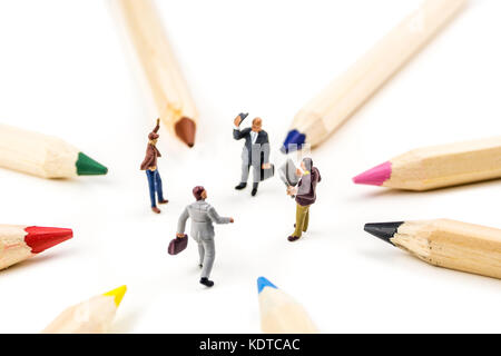 closeup of miniature figurines of businessmen having a meeting in a circle formed by multicolored pencils on white background Stock Photo