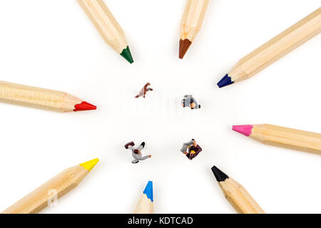 closeup of miniature figurines of businessmen having a meeting in a circle formed by multicoloured pencils on white background Stock Photo