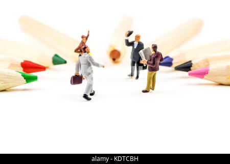 closeup of miniature figurines of businessmen having a meeting in a circle formed by multicolored pencils on white background Stock Photo