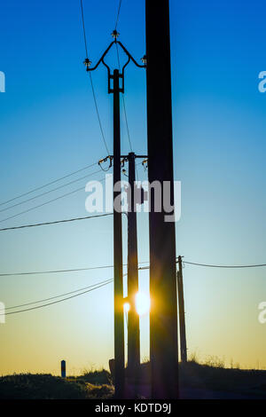 Sunrise thgrough silhouetted power poles - France. Stock Photo