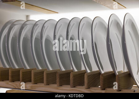 Ceramic white plates on wooden shelf in a row closeup Stock Photo