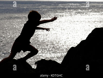A little boy (5 yrs old) leaping across rocks on the shore of the St Lawrence river at Cap Rouge near Quebec City, Canada Stock Photo