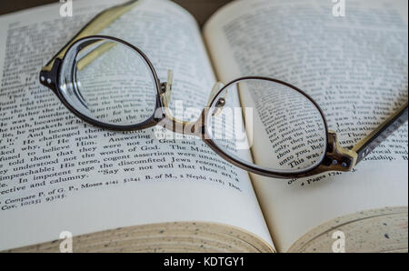 upside down pair of glasses resting on an open religious book Stock Photo