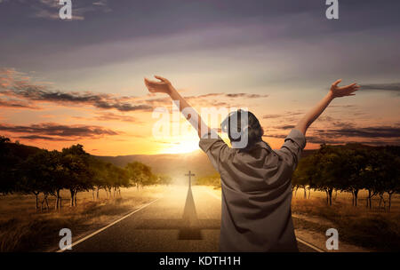 Back view of woman raising hand with open palm while praying over sunset background Stock Photo