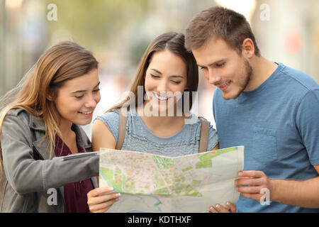 Three happy tourists consulting a paper map to find a location on the street Stock Photo