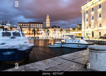 A night view of Split harbor, with boats captured with blurred motion, and the old town with the Cathedral of San Duje in the background in Croatia Stock Photo