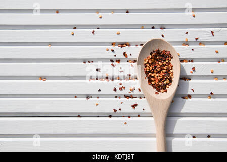 bright food photography image of new wooden spoon with colored chili flakes on white wood background in the sunshine taken on South coast England UK Stock Photo