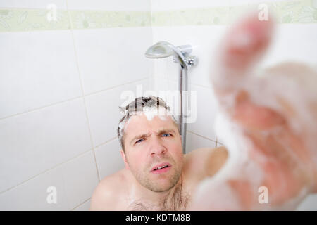 A young caucasian man takes a shower and notices a hidden camera. Stock Photo