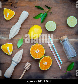 Mixed fresh citrus fruits and orange leaves background. Ingredients for summer citrus juice with juicer and glass bottle .Fresh lemons, lime and orang Stock Photo