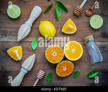 Mixed fresh citrus fruits and orange leaves background. Ingredients for summer citrus juice with juicer and glass bottle .Fresh lemons, lime and orang Stock Photo