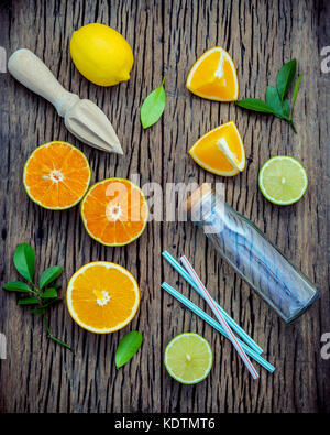 Mixed fresh citrus fruits and orange leaves background. Ingredients for summer citrus juice with juicer and glass bottle .Fresh lemons, lime and orang Stock Photo