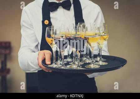 Professional waiter in black uniform serving red and white wine. Catering is serving wine and juice on a plate at business party or business event par Stock Photo