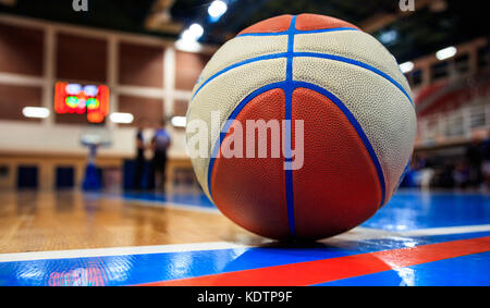Basketball ball on court floor close up with blurred arena in the background and two defocused coaches talking on court. Stock Photo