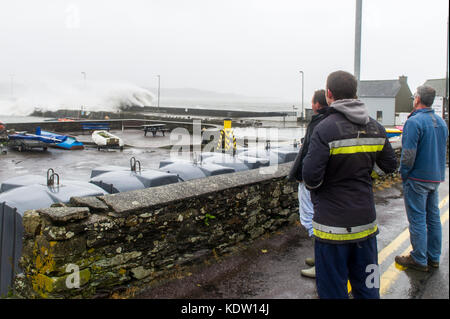 Schull, Ireland 16th Oct, 2017.  Ex-Hurricane Ophelia hits Schull, Ireland with winds of 80kmh and gusts of 130kmh.  Major structural damage is expected as the worst is yet to come. A group of local fishermen watch the waves crash over Schull pier. Credit: Andy Gibson/Alamy Live News. Stock Photo
