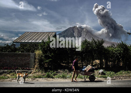 Karo, North Sumatra, Indonesia. 16th Oct, 2017. The villagers of Tiga Pancur walk near the volcano of Mount Sinabung which spewed dust as seen in Karo, North Sumatera province. Thousands were evacuated after Mount Sinabung started erupting and spewing ash half a kilometre into the air. The volcano began erupting in 2010 after lying dormant for four centuries. A large eruption in May 2016 killed seven people. Credit: Ivan Damanik/ZUMA Wire/Alamy Live News Stock Photo