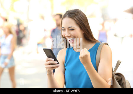 Excited woman reading amazing news on line in a smart phone on the street Stock Photo