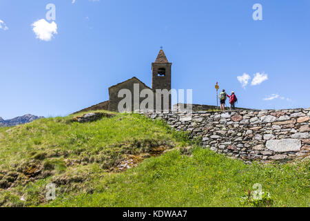 Hikers at the ancient church of San Romerio Alp, Brusio, Canton of Graubünden, Poschiavo valley, Switzerland Stock Photo