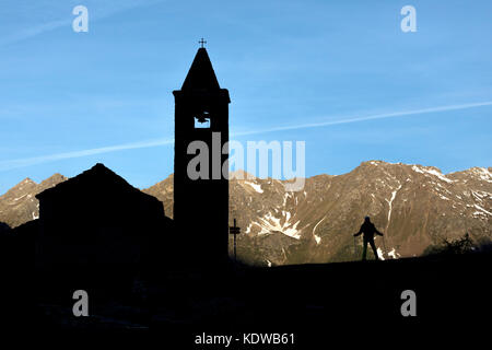 Silhouette of hiker at the old church at dawn, San Romerio Alp, Brusio, Canton of Graubünden, Poschiavo valley, Switzerland Stock Photo