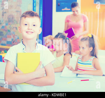 Glad boy pupil standing in elementary school class with textbook in hands Stock Photo