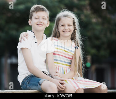 Two smiling kids in elementary school age hugging each other in town Stock Photo