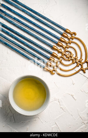 Menorah brass Hanukkah with blue candles and butter in a bowl on a white table vertical Stock Photo