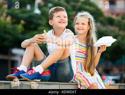 cheerful girl and boy sitting together in park on warm summer day Stock Photo