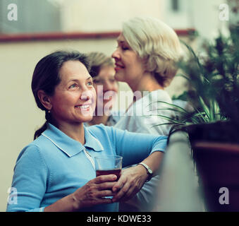 Three happy smiling mature women resting with tea at balcony. Focus on brunette Stock Photo