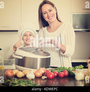 Slow cooker helping mother and smiling girl to prepare dinner at home kitchen Stock Photo
