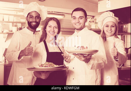 happy waitress and crew of professional cooks posing at restaurant kitchen Stock Photo