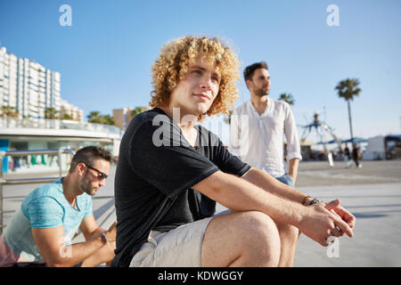 Portrait of young handsome man sitting outside with friends waiting Stock Photo