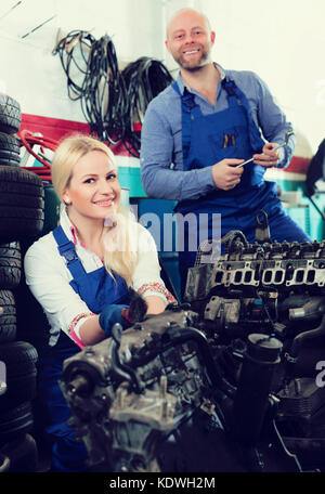 Portrait of two smiling troubleshooters near car indoor. Focus on woman Stock Photo