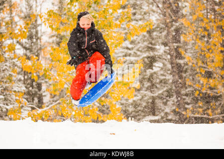 A boy leaps onto his disc while snow sledding during a late autumn snowfall in Redwood Meadows, Alberta, Canada.