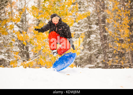A boy leaps onto his disc while snow sledding during a late autumn snowfall in Redwood Meadows, Alberta, Canada.