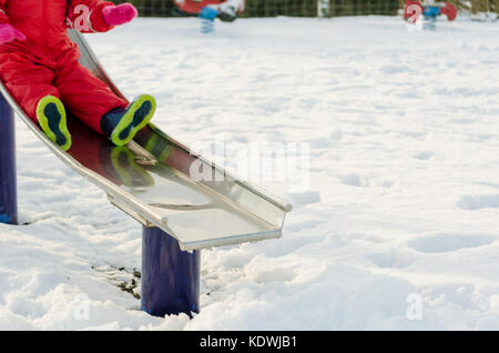 Kid playing outdoors in the snow. Active winter lifestyle. Preschooler child on a slide in a playground with motion blur Stock Photo
