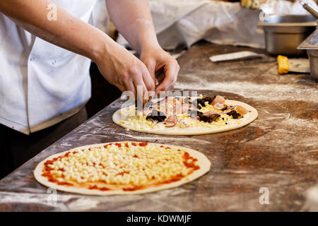 Cook putting toppings on two pizzas. Stock Photo