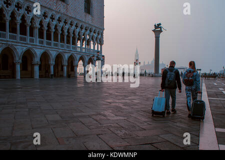 VENICE, ITALY - OCTOBER 6, 2017: Two tourists with suitcases go over the Piazza San Marco, morning Stock Photo