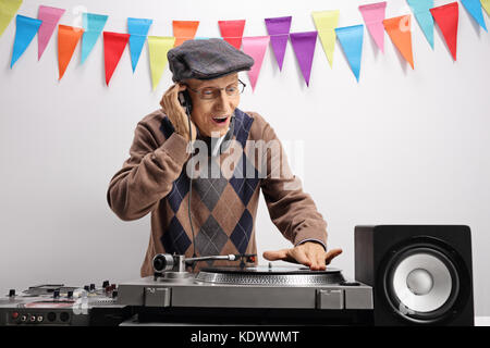 Elderly DJ playing music on a turntable against a wall with decoration flags Stock Photo