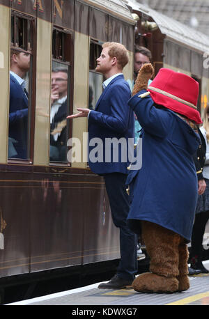 Prince Harry stands with a costumed figure of Paddington bear as he speaks to children onboard the Belmond British Pullman train on platform 1 at Paddington Station, London, as he attends the Charities Forum event, joining children from the charities he supports and to meet the cast and crew from the forthcoming film Paddington 2. Stock Photo