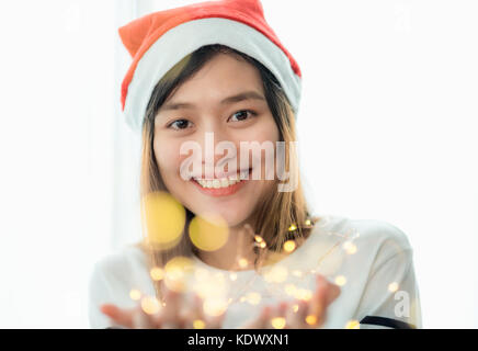 smiling asia woman wear santa hat holding party string lights with bokeh light at Christmas party,Holiday celebration concept,sparkling light decorati Stock Photo