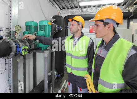 Two workers in hardhats at plant checking parameters of pressure Stock Photo