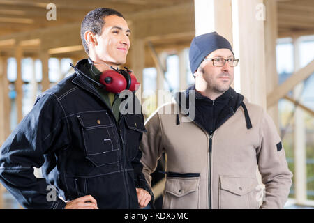Confident male carpenters in jackets looking away while standing at site Stock Photo