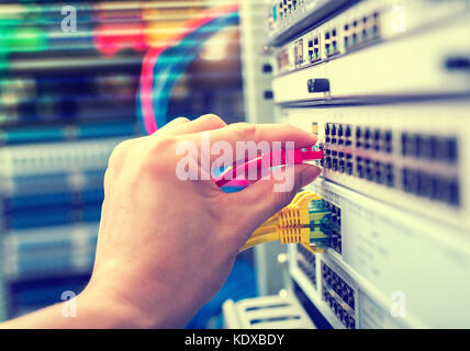 administrator holding network cables connected to servers Stock Photo