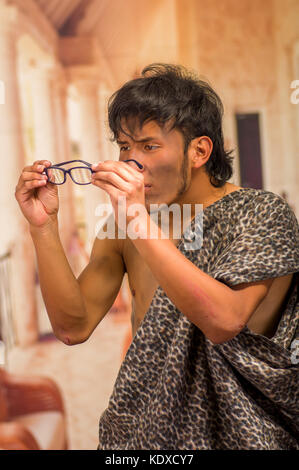 Close up of funny prehistoric man doing funny faces to the camera, holding in his hands a glasses, in a blurred background Stock Photo