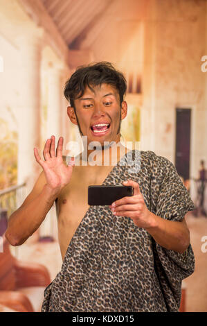 Close up of funny prehistoric man doing funny faces to the camera, doing a videocall using his cellphone, in a blurred background Stock Photo