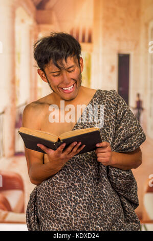 Close up of funny prehistoric man smiling to the camera, reading a book in a blurred background Stock Photo