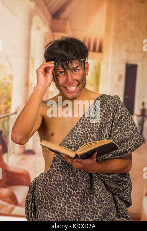 Close up of funny prehistoric man smiling to the camera, wearing glasses and reading a book in a blurred background Stock Photo